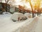 Cars covered with snow on winter street in sunset
