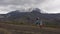 Cars drive along mountain road and group hikers walk at foot of active volcano