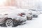 Cars parked in row at outdoor parking in winter. Vehicles covered by snow during heavy snowfall. snowstorm or blizzard weather