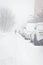 Cars parking under heavy snow on the street. City storm.