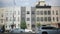 Cars pass in front of multicolored Brooklyn row houses with cars parallel parked in front