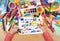 Cartoon game toy and people collection child drawing , top view hands with pencil painting picture on paper, artwork workplace