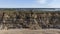 A cartoon look of an aerial view of a coastguard tower on the top of a hill with eroded cliff along a sandy beach with an harbor