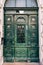 Carved green wooden doors with glass, pillared and narrow, outside in the facade of a building on a street in Budapest