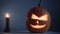 Carved Halloween pumpkin lights inside with flame on a dark blue background with lighted candles close up.