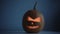 Carved Halloween pumpkin lights inside with flame on a dark blue background with lighted candles close up.