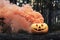 Carved halloween pumpkin with orange smoke on tree trunk in forest