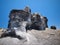 A carved rock sculpted by wind erosion against background of deep blue sky. Black lava gravel