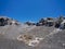 A carved rock sculpted by wind erosion against background of deep blue sky. Black lava gravel