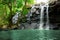 Cascading waterfall in rainforest falls into blue pool