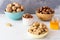 Cashews in shell, hazelnuts in shell, walnuts in shell and peeled in different bowls are on a white table against a gray wall.