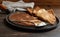 Cast-iron pan with baked thin pancakes and a spoon with sour cream on a dark wooden surface, close-up