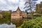 Castle of Het Oude Loo with its bridge reflected in the water surface of its moat among trees and green vegetation