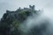 A castle sits atop a mountain covered in dense fog, creating an eerie and mysterious atmosphere, Ancient castle ruins on a mist-