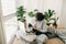 Casual girl working on laptop with her cat, sitting together in modern room with pillows and plants. Cute cat helping owner during