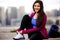 Casual lifestyle portrait of beautiful Indian American woman relaxing after cardio fitness exercise, city skyline buildings in bac