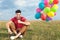 Casual man sitting on the grass with balloons