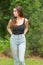 Casual young female model posing in tank top in a nature woods scene hands in back pockets