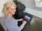 A casually dressed caucasian middle aged woman is installing a laptop computer with a stack of several more computers