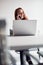 Casually Dressed Young Businesswoman Working On Laptop At Desk In Modern Workplace Making Phone Call