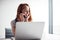 Casually Dressed Young Businesswoman Working On Laptop At Desk In Modern Workplace Making Phone Call