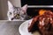 Cat close-up glances at piece meat. Pet watch from behind kitchen table. Grey cat looks at background of kitchen and a large piece