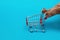 Cat paws push an empty shopping trolley on a blue background