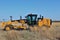 A Cat road grader in a field with prairie grass and blue sky out in the country