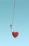 Catching love concept. Hooked red shiny heart hanging on pink thread on a blue background.
