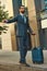 Catching taxi. Full length of young and handsome bearded man in suit carrying suitcase and raising his arm while