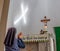 Catholic nun praying the rosary in front of crucifix with beam of light creating a cross on the wall.