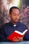 Catholic priest wearing traditional clerical collar shirt sitting and holding bible while reading, religion concept