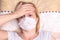 Caucasian adult woman lying in bed with flu, cold and fever, she is sick and wearing face mask