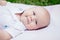 Caucasian baby boy with blue grey eyes lying on grass in park
