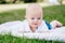 Caucasian baby boy with blue grey eyes lying on grass in park