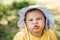 Caucasian baby girl is grimacing to the camera in hat and yellow dress. Summer childhood