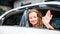 Caucasian beautiful female with a little smile sitting inside the car and waving her hand outside car window. Automobile rental