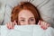 Caucasian beautiful redhaired ginger woman hidden under white duvet looking at camera , top view