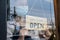 Caucasian beautiful waitress wear mask, turns open sign on glass door. Attractive Coffee shop owner prepare to welcome customer to