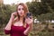 Caucasian beautiful woman in casual but sexy outfit standing in park, outdoor, holding her phone in her arms and make dumb selfie