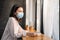 Caucasian beautiful woman customer wear face mask due to Covid 19 pandemic, keep distance sit alone in coffeehouse shop. Young