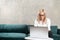 Caucasian beautiful woman working remotely online with laptop on the green sofa. Freelance video call of businesswoman