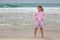 Caucasian blond baby girl in pink stands on the beach