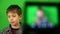Caucasian boy in front of the camera records online video, sitting against the background of green cloth. Out of focus in front of