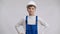 Caucasian boy in hard hat and overalls putting hands on hips posing at white background. Medium shot portrait of