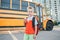 Caucasian boy student with backpack near yellow bus on first September day. Child kid eating apple fruit at school yard outdoors.