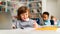 Caucasian boy studying with laptop and writing in notepad, sitting at table in classrom with diverse classmates