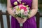 Caucasian bridesmaid wearing a beautiful purple gown and holding a bridal round bouquet