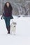 Caucasian Brunette Woman Along With Her Husky Dog Walking Outdoors in Winter Forest.Focus on The Dog