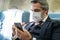 Caucasian businessman wearing face mask using mobile phone on airplane during covid pandemic to prevent coronavirus infection. The